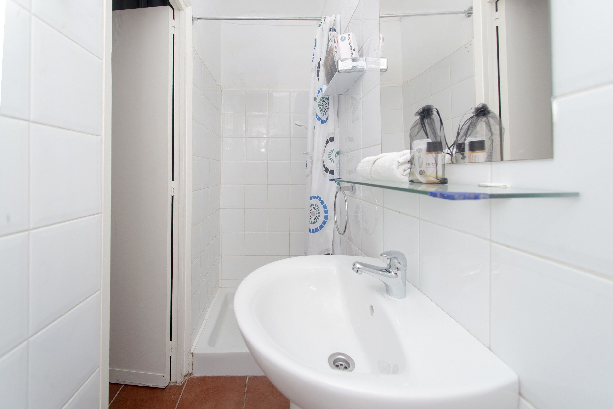 Een badkamer met een witte wastafel, een douche en een glazen plank met toiletartikelen.
