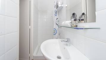 Een badkamer met een witte wastafel, een douche en een glazen plank met toiletartikelen.