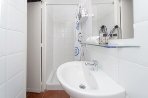 Een badkamer met een witte wastafel, een douche en een glazen plank met toiletartikelen.