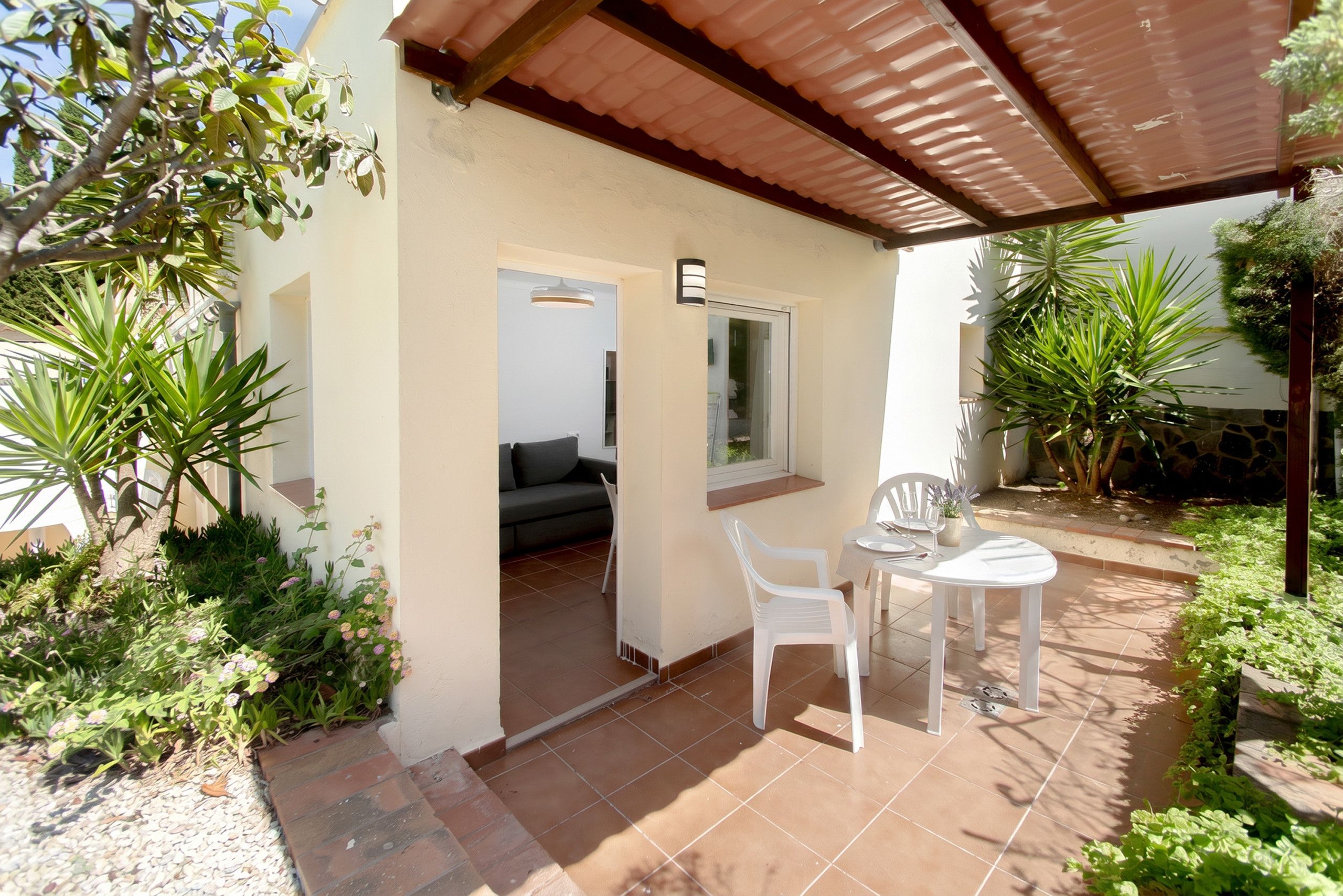 Un patio con mesa y sillas, un sofá y un acceso interior por un ventanal corredero.