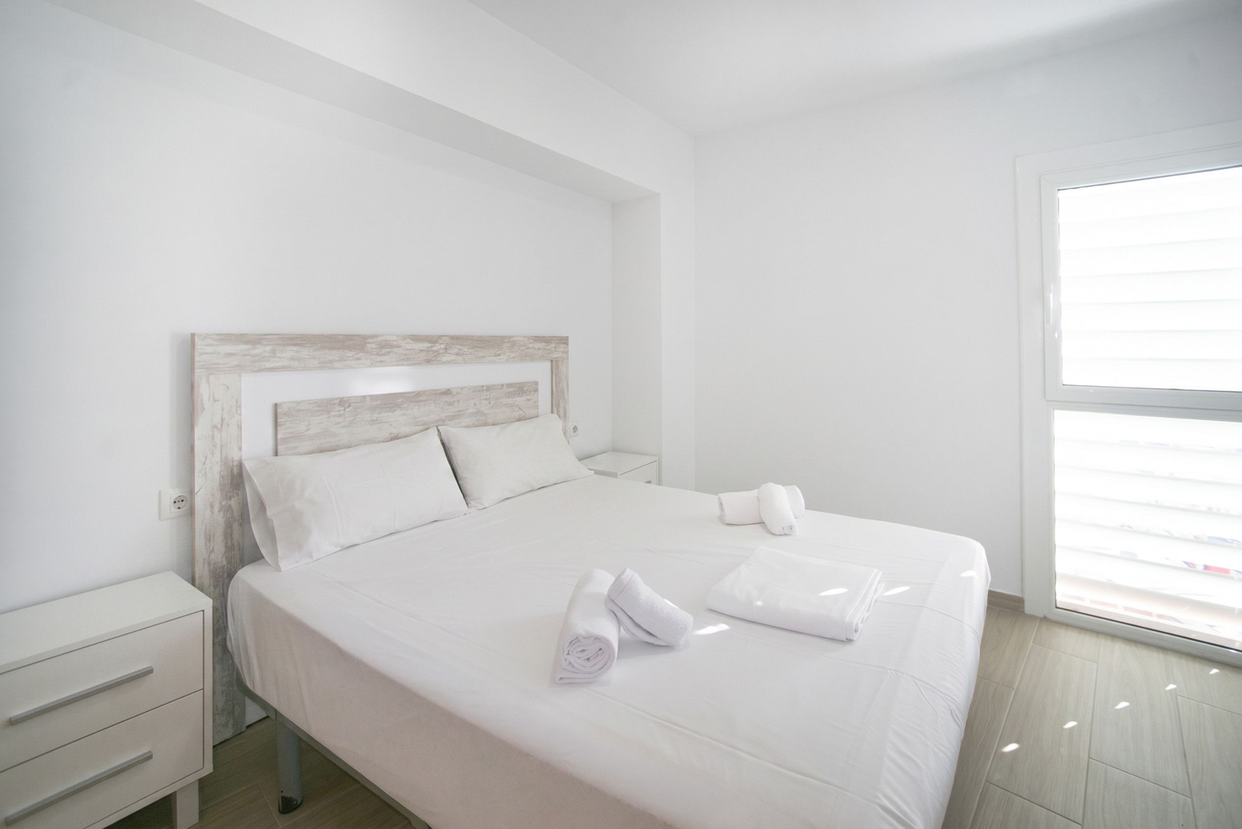A hotel room with a bed, a nightstand, a window, and a view of the outside.