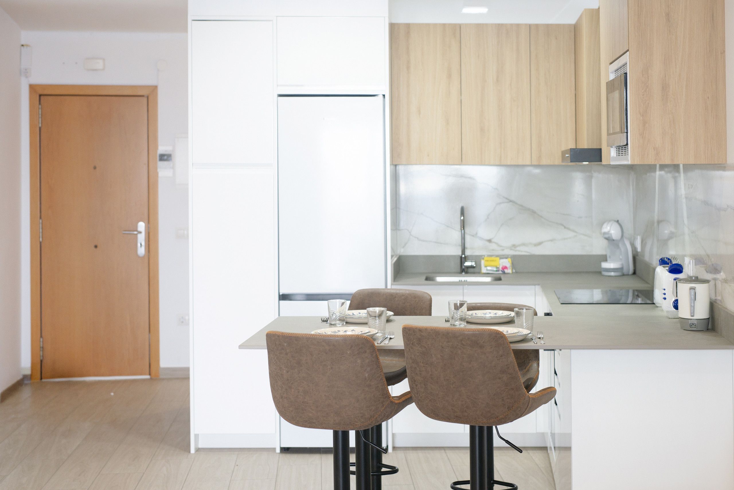 Cocina moderna con comedor, que incluye una puerta de madera, armarios blancos y un salpicadero de mármol.