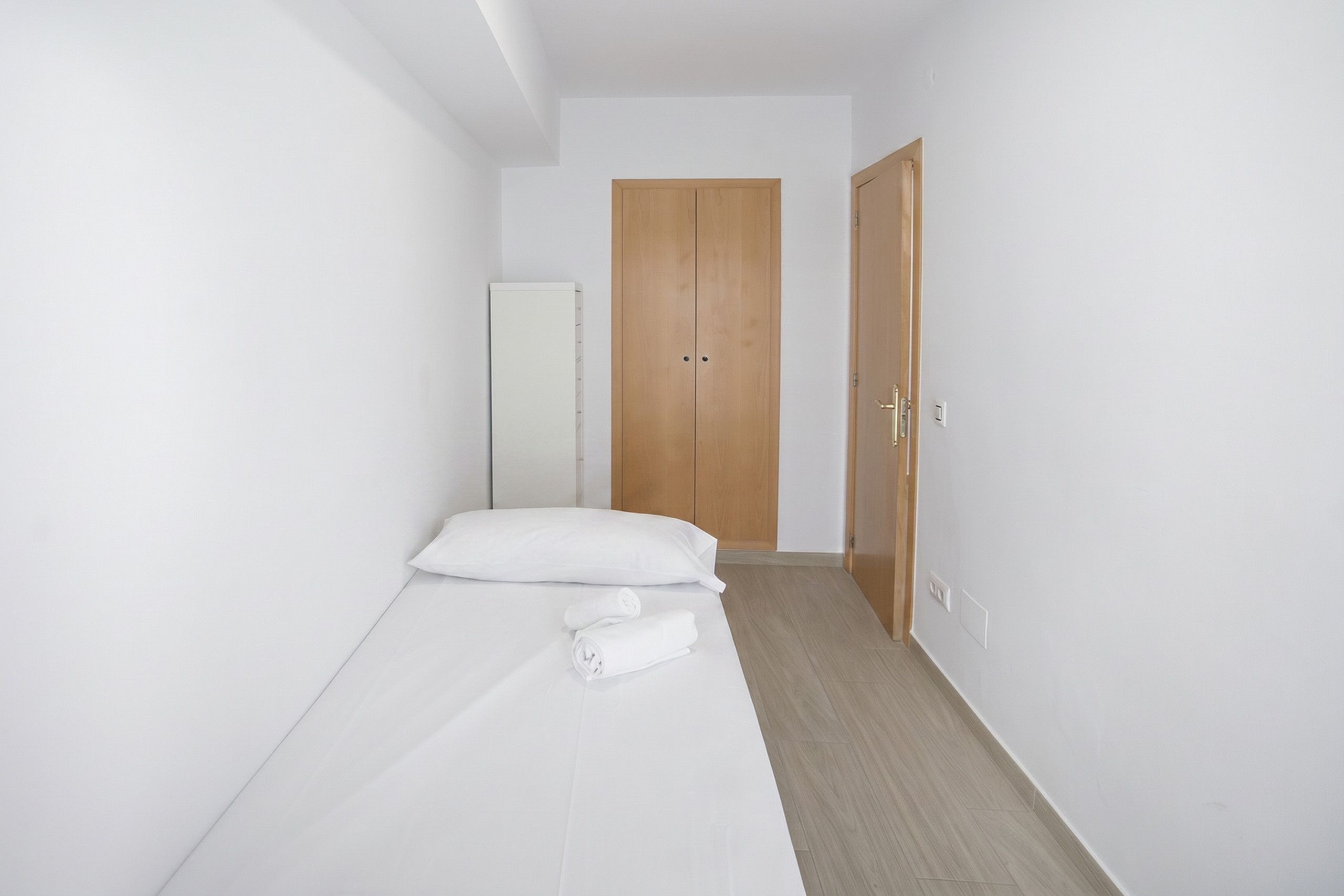 Una habitación pequeña y limpia con una cama individual, un armario y una puerta.