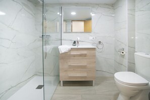 Um banheiro moderno com box de vidro, toucador de madeira com espelho e vaso sanitário branco.