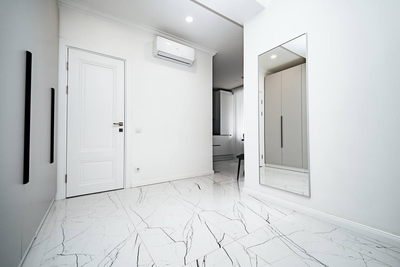 Un couloir aux murs blancs, une porte blanche et une armoire blanche avec un miroir.