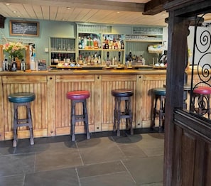 Un espace bar avec des tabourets en bois, un comptoir et des étagères remplies de bouteilles et de verres.