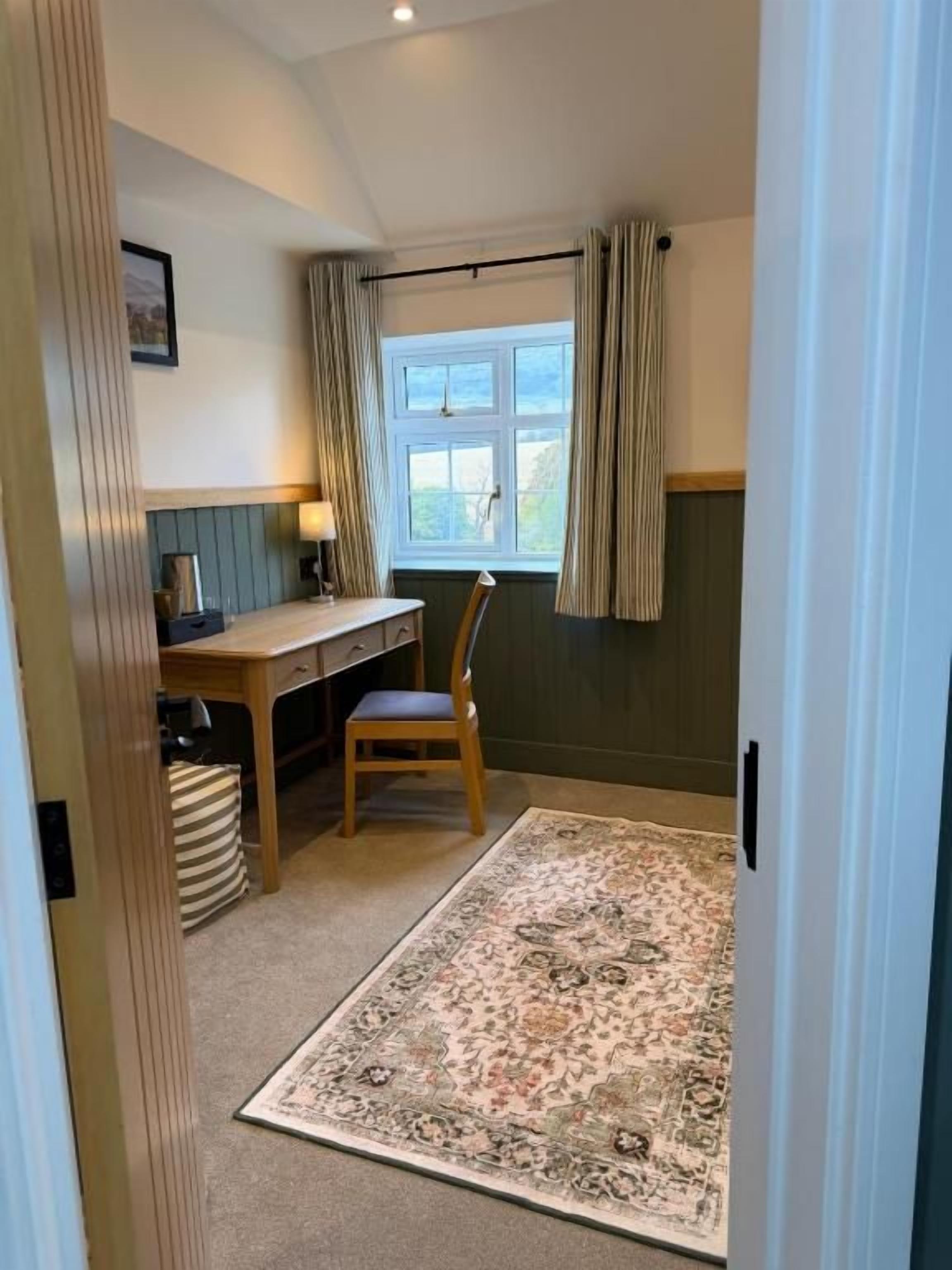 Una habitación con escritorio, silla y ventana con cortinas.