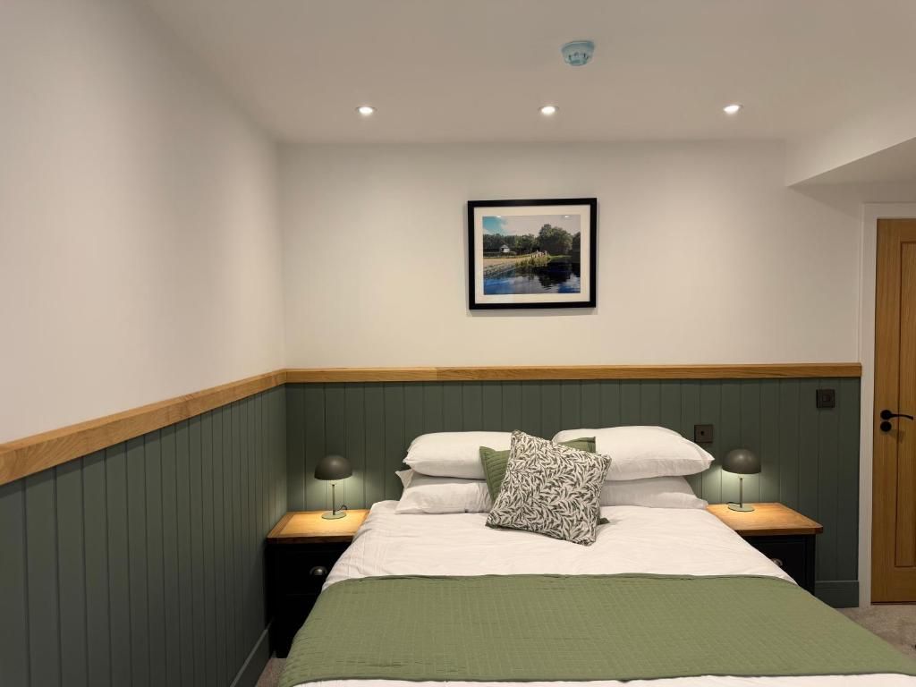 Un dormitorio con una cama, dos mesitas de noche, una lámpara de noche, una manta verde y un cuadro en la pared.