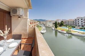 Ein Balkon mit Esstisch, der auf einen Kanal mit Booten und einen Swimmingpool blickt.