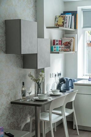 A modern kitchen with white cabinetry, a dining table with chairs, and a window with natural light. - Modern studio apt in West Hampstead London 2 (London)