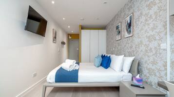 A modern bedroom with a bed, a TV mounted on the wall, and a bedside table with a remote control.