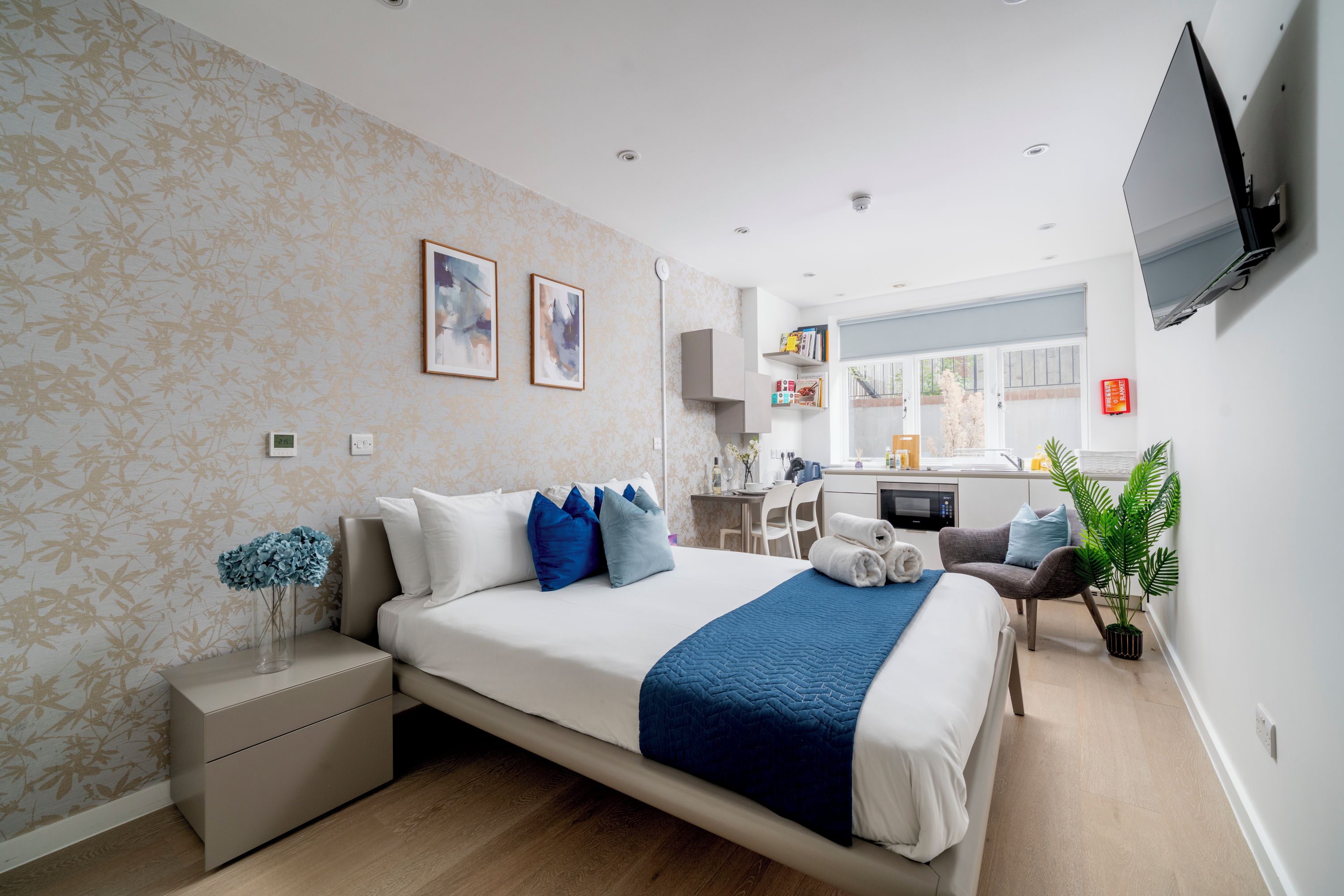 A modern hotel room with a bed, bedside table, and a view of the kitchen.