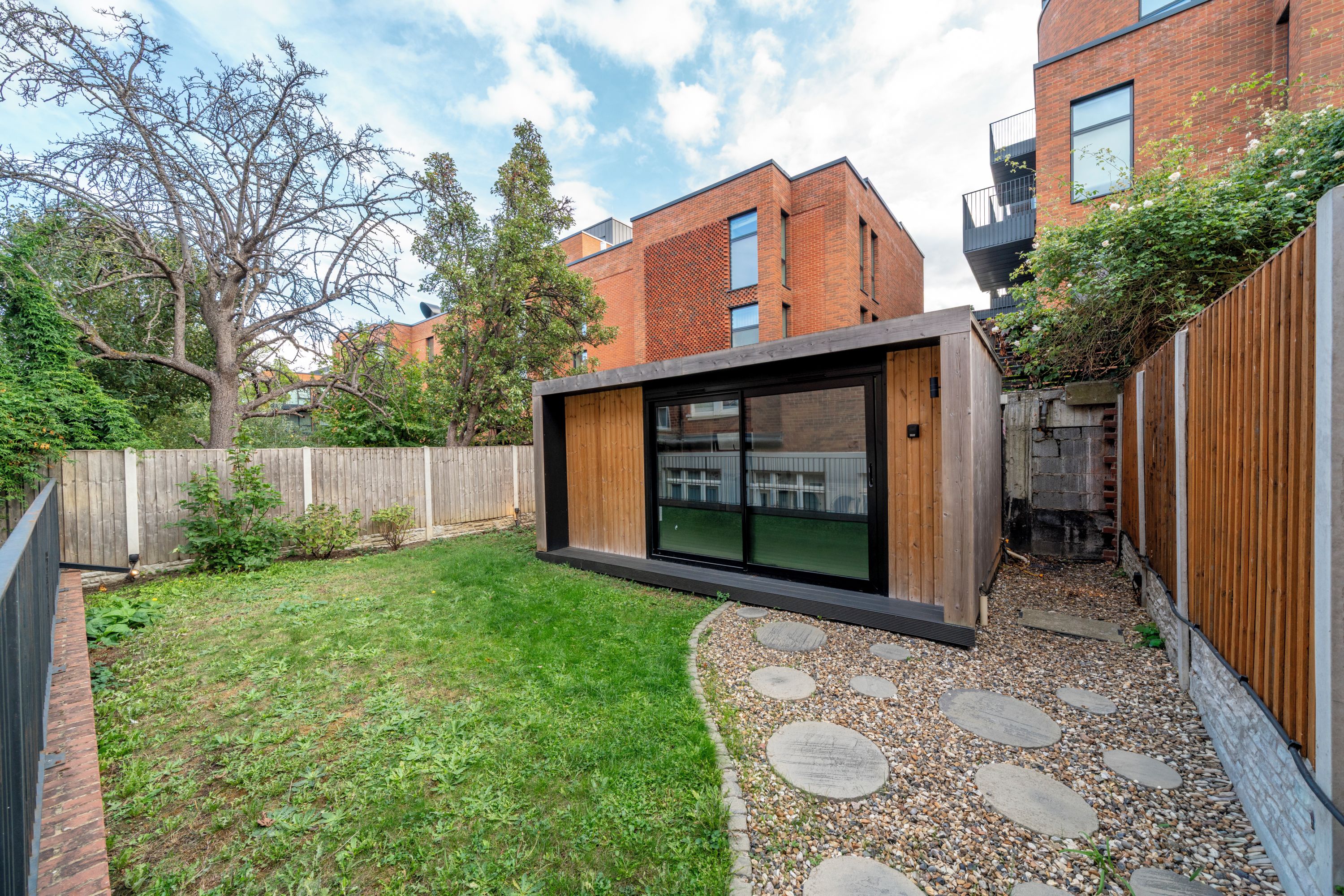 A modern outdoor space with a wooden deck, a grassy lawn, and a stone pathway.