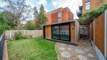 A modern outdoor space with a wooden deck, a grassy lawn, and a stone pathway.