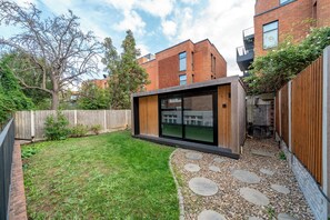 A modern outdoor space with a wooden deck, a grassy lawn, and a stone pathway. - Modern studio apt in West Hampstead London 2 (London)