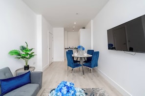 Ett modernt vardagsrum med en grå soffa, en blå prydnadskudde, ett runt soffbord med en blå blomsteruppsättning och en matplats med blå stolar och ett vitt bord.