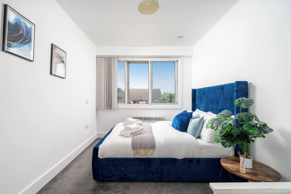 Un dormitorio moderno con una cama grande, una ventana con vistas y una planta en maceta.