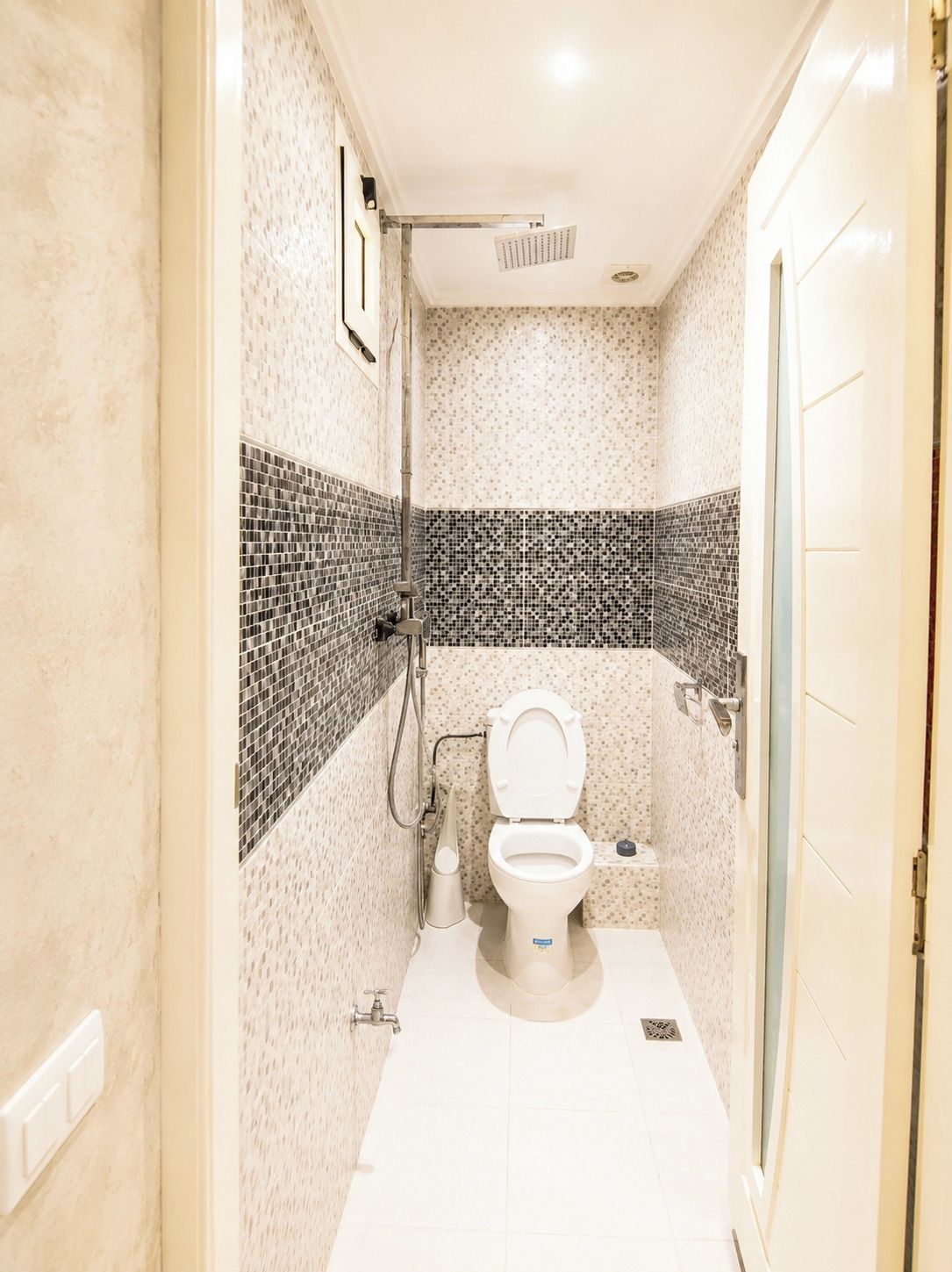 Un baño pequeño y estrecho con inodoro, ducha y pared de azulejos.