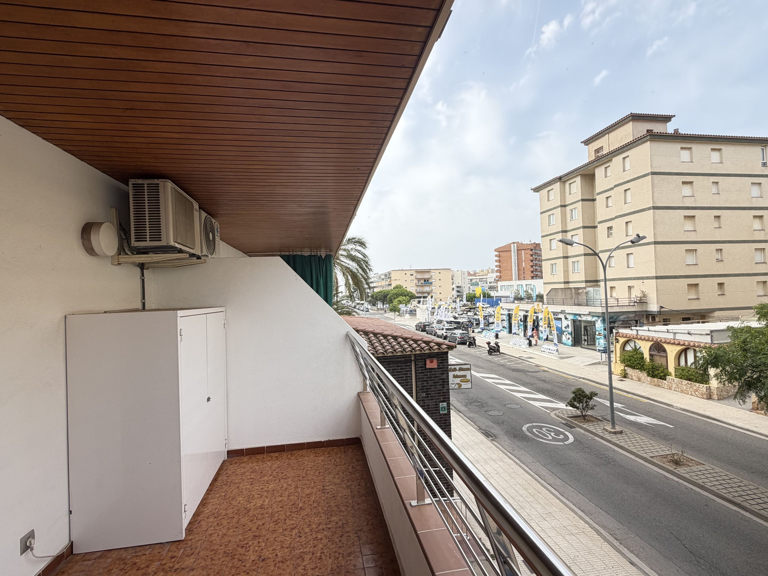 Een balkon met uitzicht op een stadstraat, een witte deur en een airconditioning.