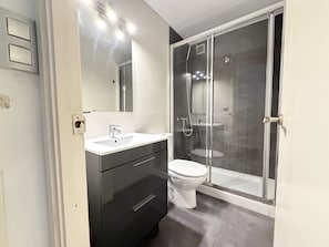Un baño moderno con ducha de vidrio, lavamanos blanco y un inodoro.