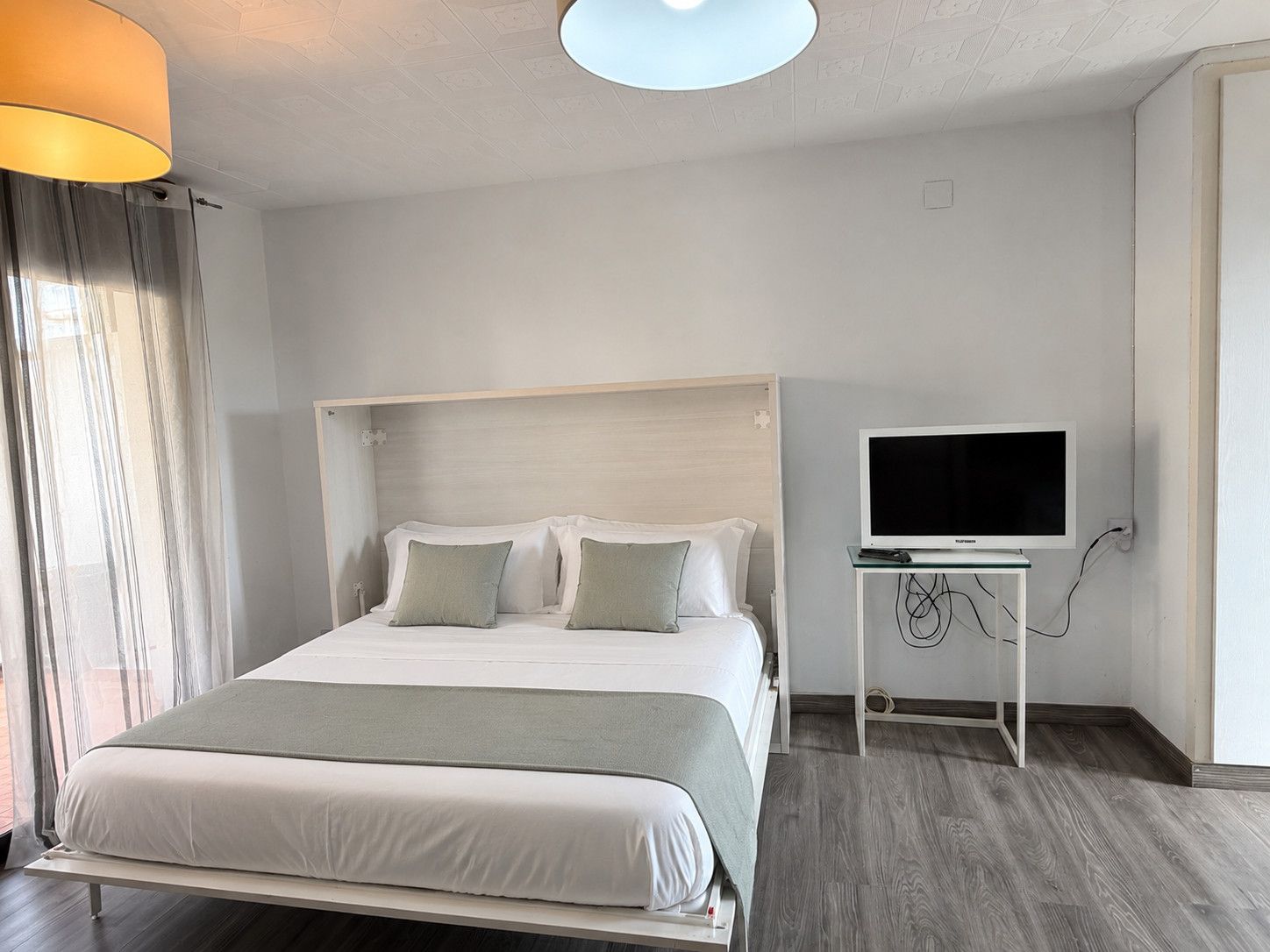 Ein Hotelzimmer mit einem Bett, einem Fernseher auf einem Schrank und einem fenster mit Vorhängen.