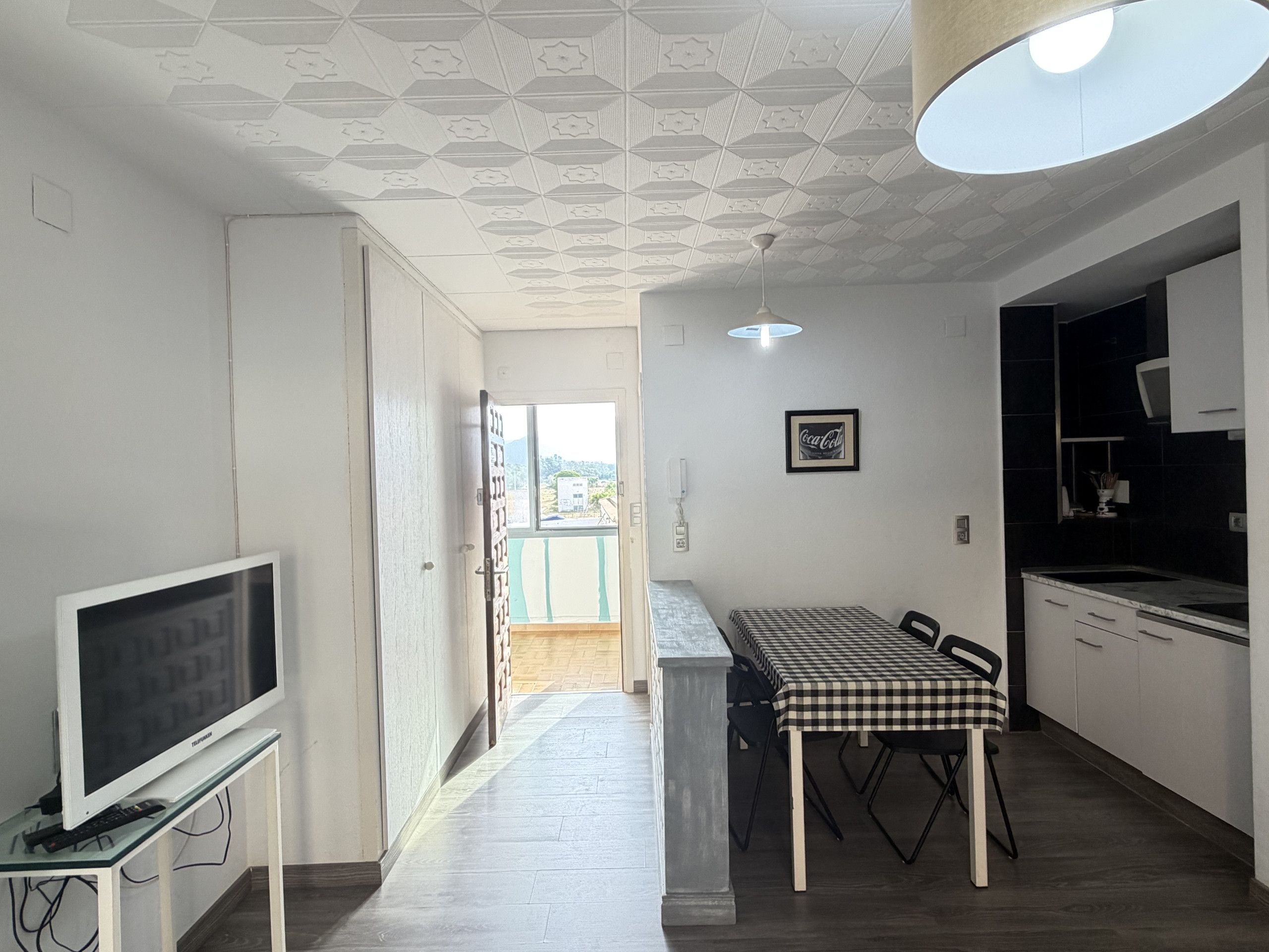 Una cocina moderna con comedor, un televisor sobre un mueble bajo y un techo con diseño geométrico.