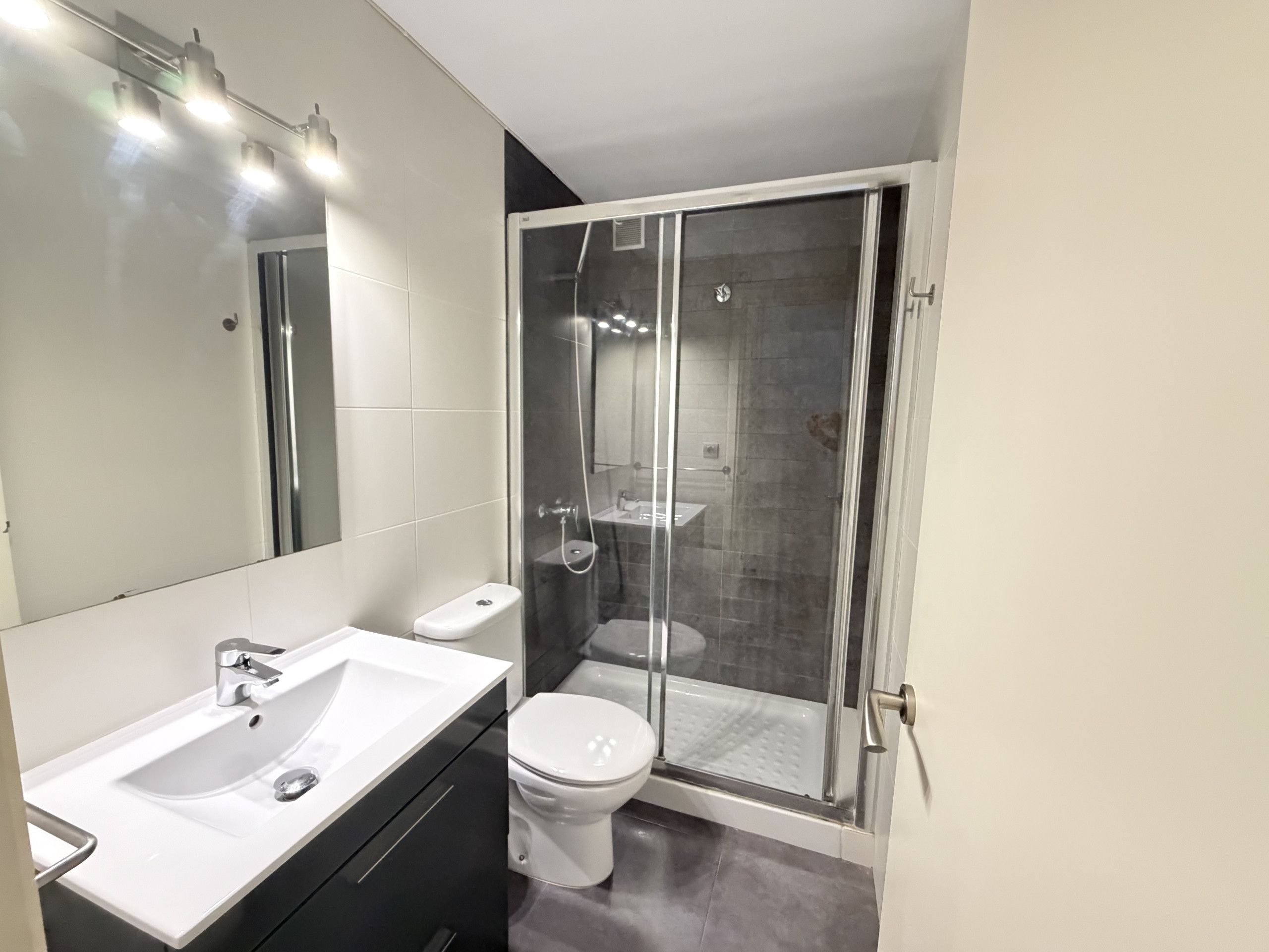Un baño moderno con lavamanos blanco, inodoro y ducha con cerramiento de vidrio.
