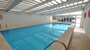 Una piscina interior con agua azul cristalina, piso de baldosas y techo con tragaluces.