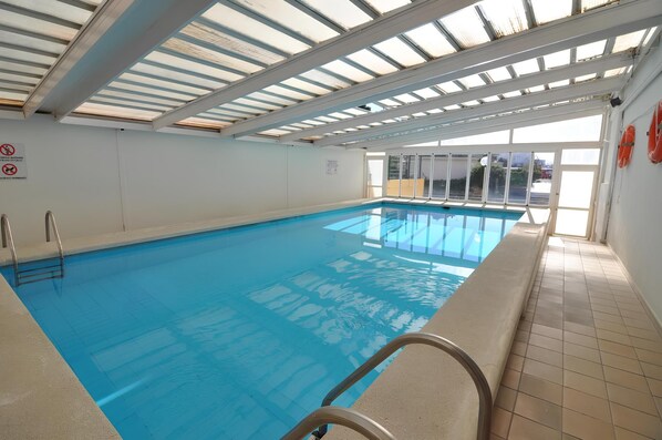 Una piscina interior con agua azul cristalina, piso de baldosas y techo con tragaluces.