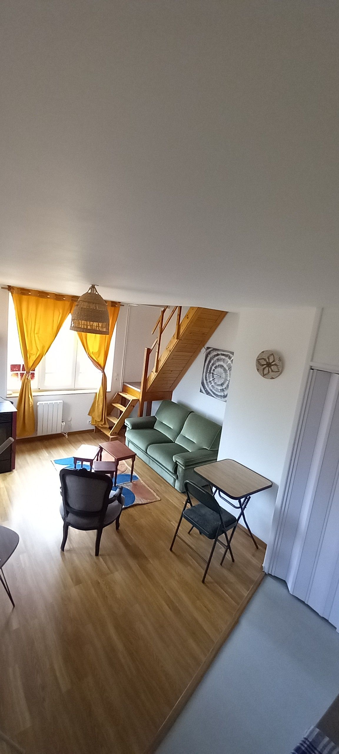 Ett vardagsrum med en grön soffa, ett litet bord, en stol och en trappa som leder upp till ett övre plan.