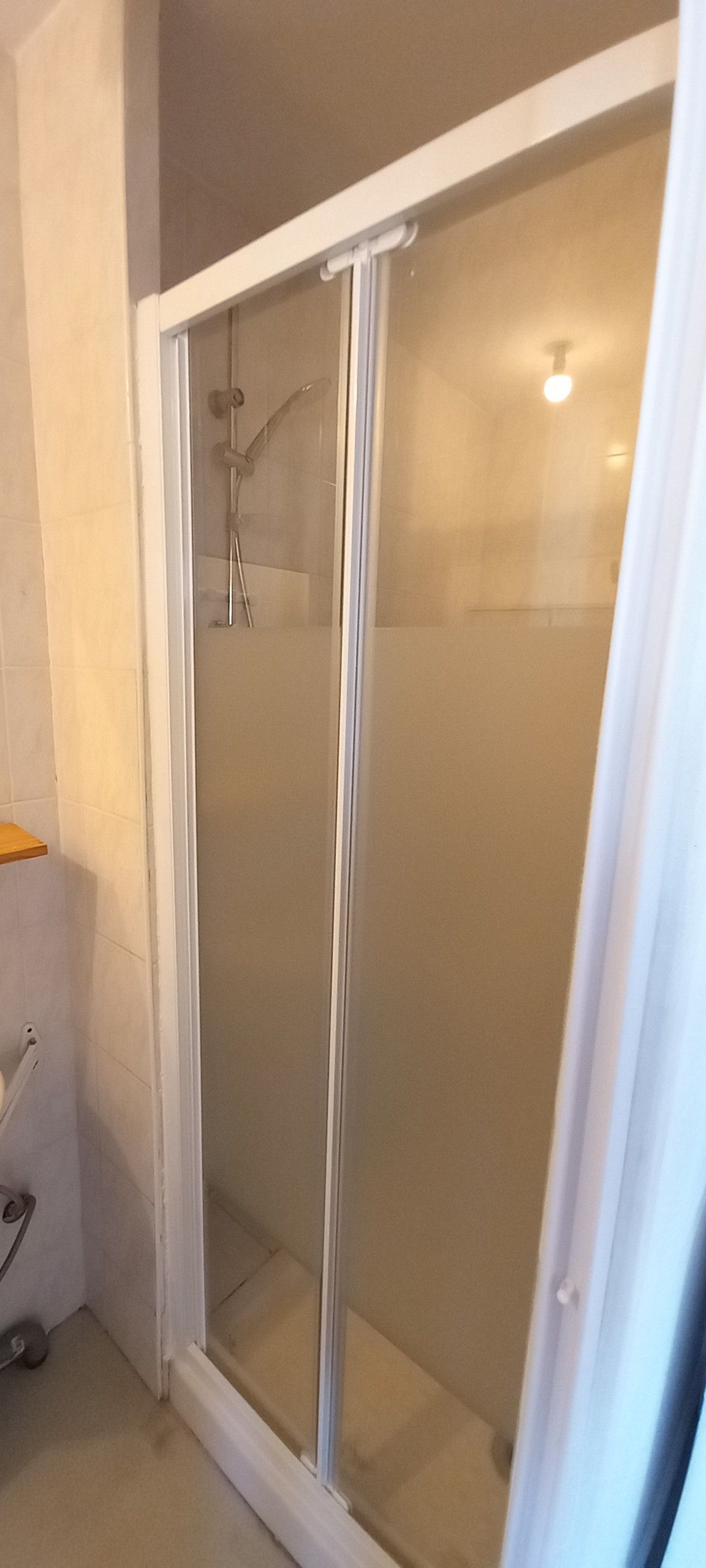 En dusch med glasväggar och en vit ram, en handduksställning och ett duschmunstycke.
