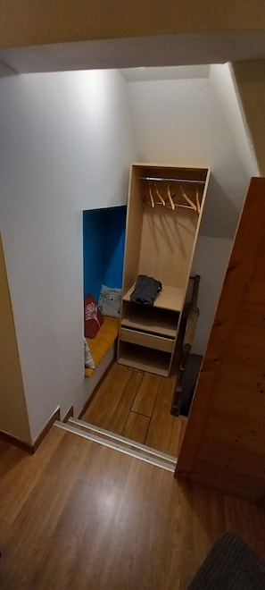 A small, narrow room with a wooden floor, a bed with a blue headboard, a wooden wardrobe, and a small seating area with cushions. - Apartment 'L'étoile De L'échappée En Thiérache' with Wi-Fi (Martigny)