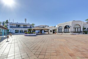 Un amplio patio con suelo de baldosas, una zona de estar cubierta y un edificio con ventanas de arco.