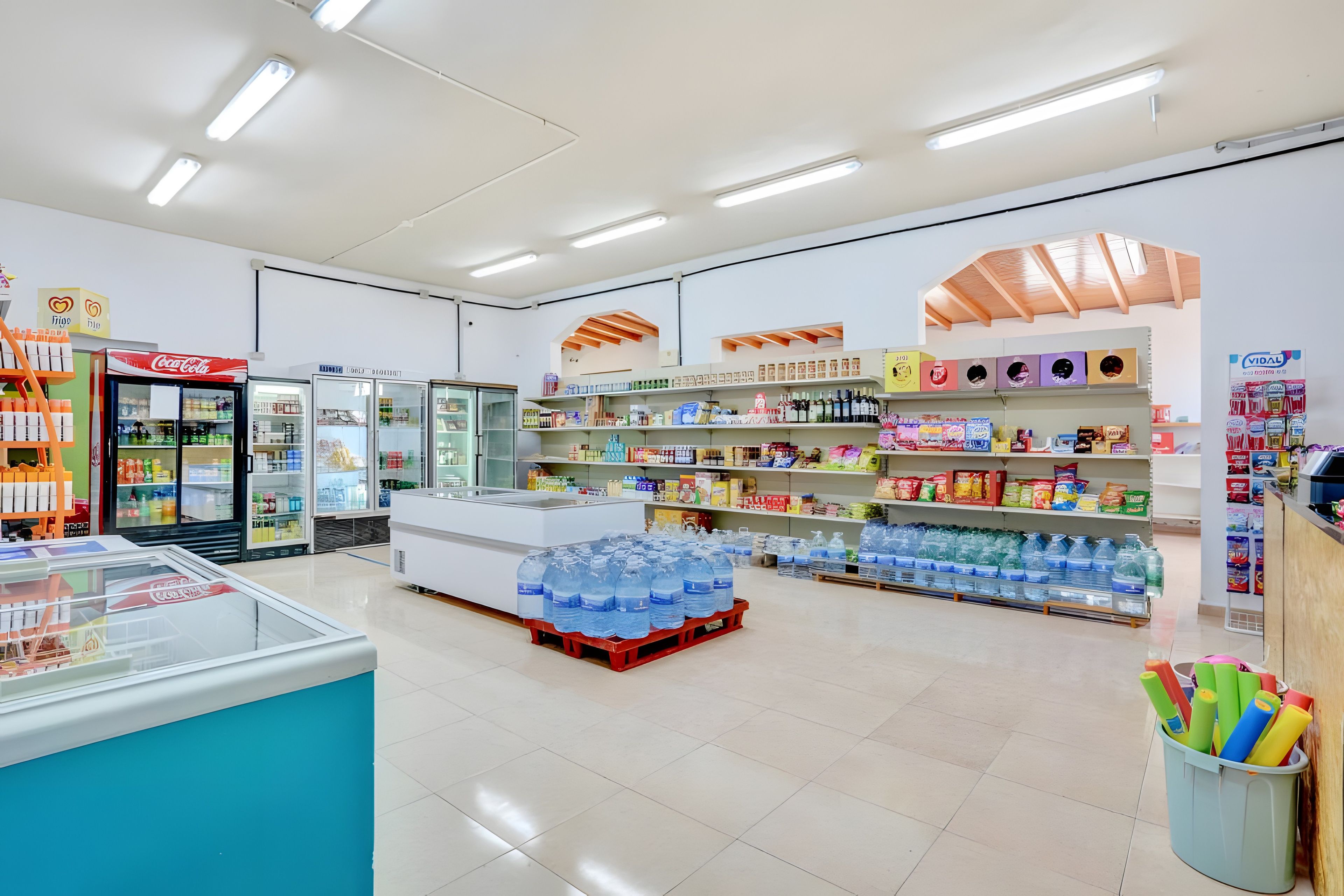 Una tienda con estantes llenos de diversos productos, un refrigerador de Coca-Cola y una exhibición de agua embotellada.