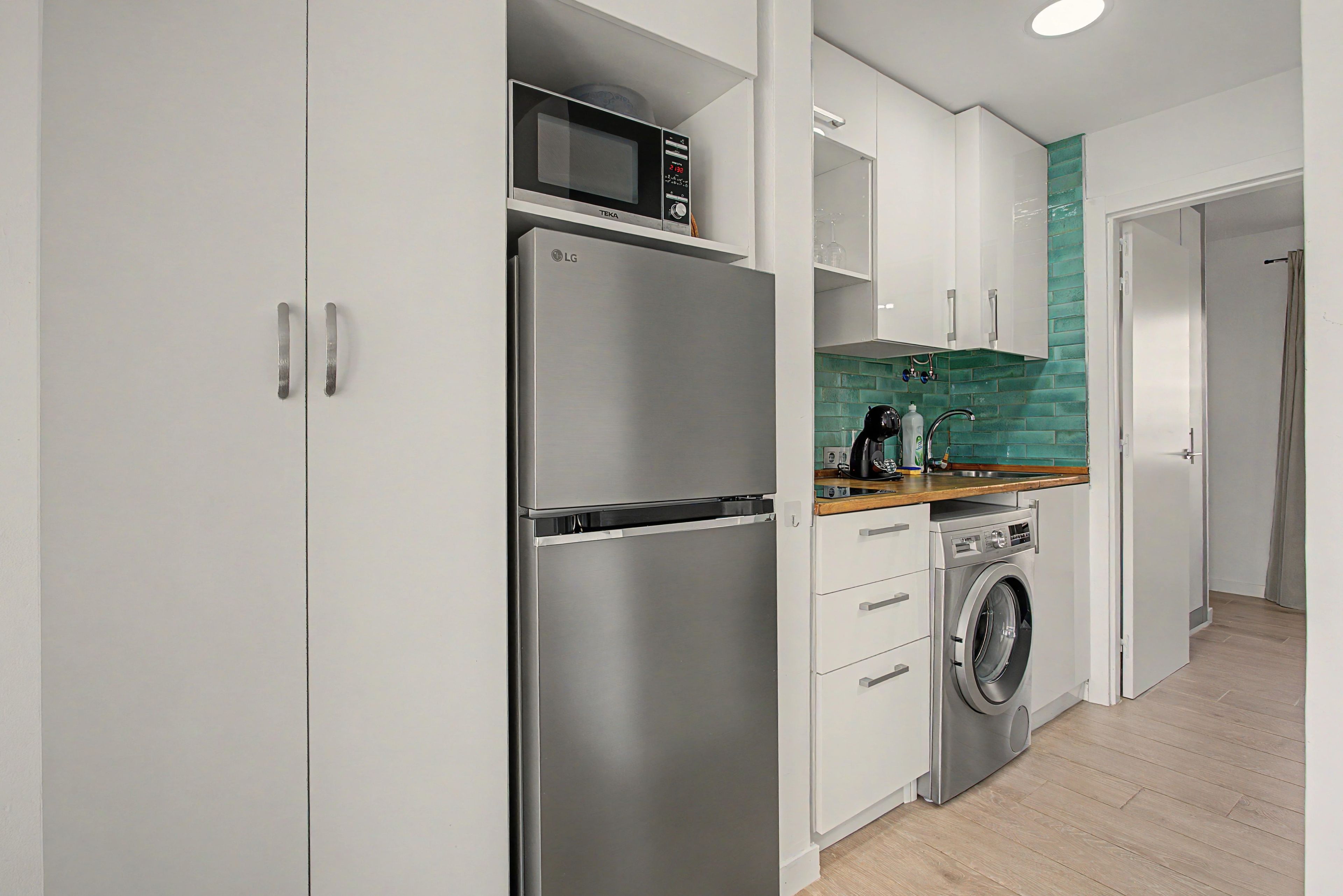 A modern kitchen with a stainless steel refrigerator, microwave, and built-in washing machine.