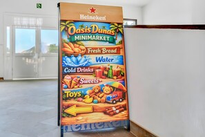 Skilt for Heineken Oasis Duna's Minimarket med kategorier som frisk brød, vand, kolde drikke, slik og legetøj.