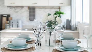 A modern kitchen with white cabinets, a marble backsplash, and a dining area set with light blue plates, bowls, and glasses.