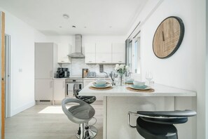 Una cocina moderna con armarios blancos, una isla central con taburetes y una pared de madera redonda.