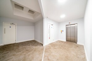 En hall med heltäckningsmatta på golvet, vita väggar och dörrar som leder in till rummen. En hiss syns till på höger sida.