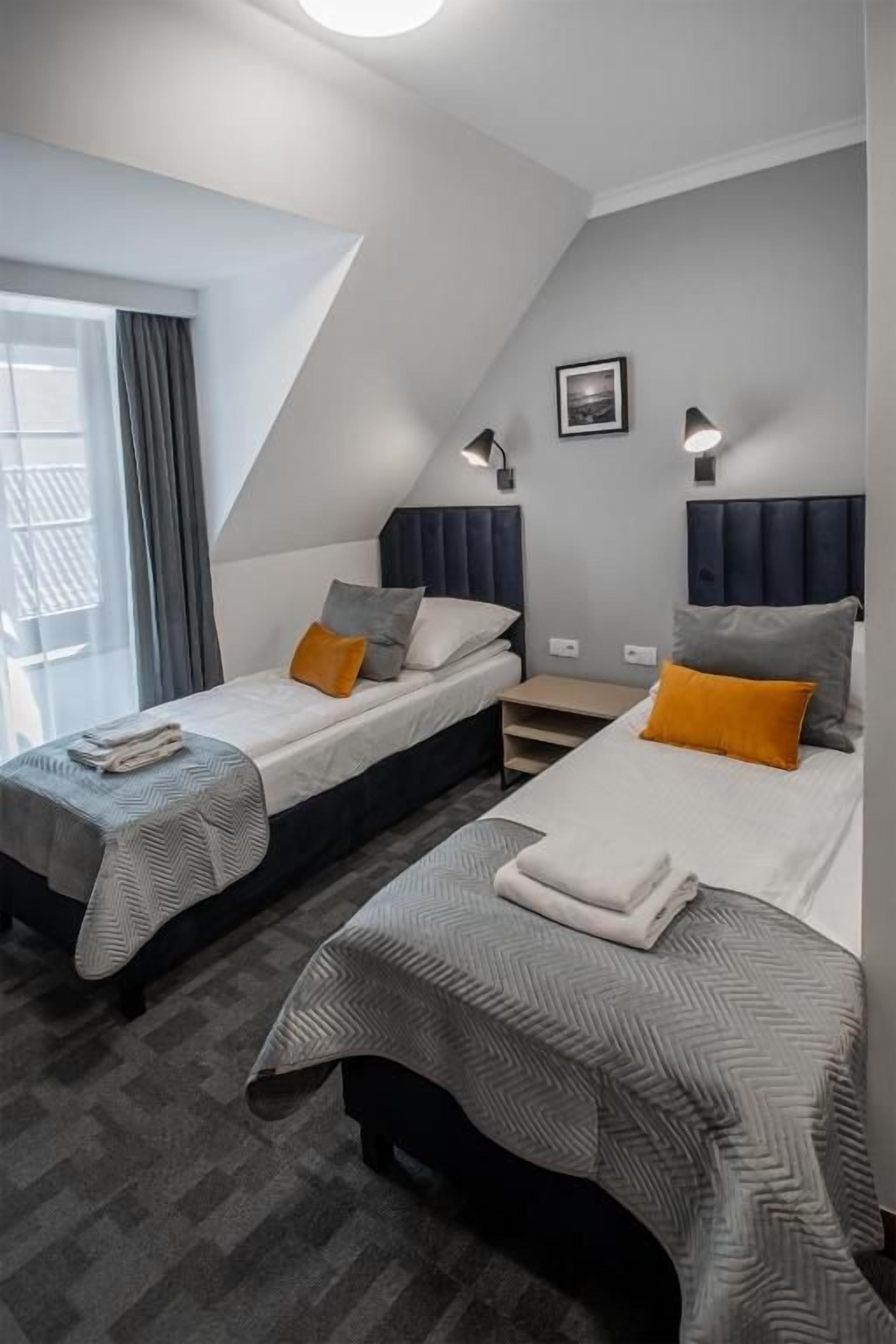 A hotel room with two beds, a window with curtains, a picture on the wall, and a bedside lamp.