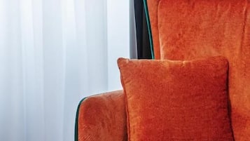 A room with a single orange upholstered chair, a small table, and a window with sheer curtains.
