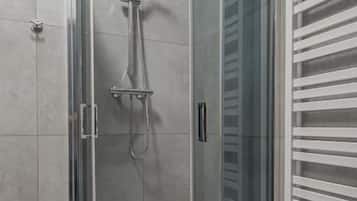 A glass-enclosed shower stall with a handheld showerhead and a wall-mounted faucet.