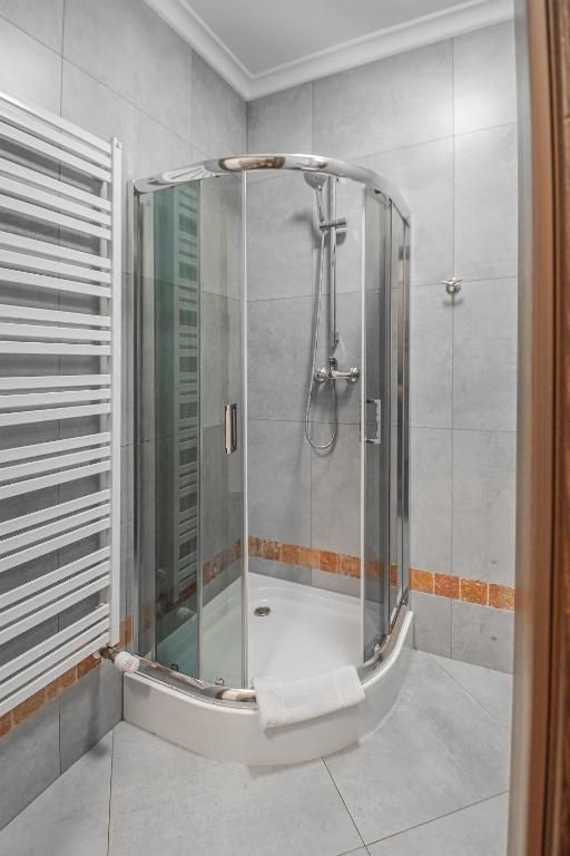 A glass-enclosed shower with a white towel on the floor, a glass door, and a corner tile design.