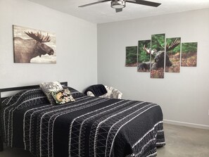 Un dormitorio con una cama, un ventilador de techo y decoración en la pared, incluyendo una pintura de alce y un conjunto de fotografías de alces.