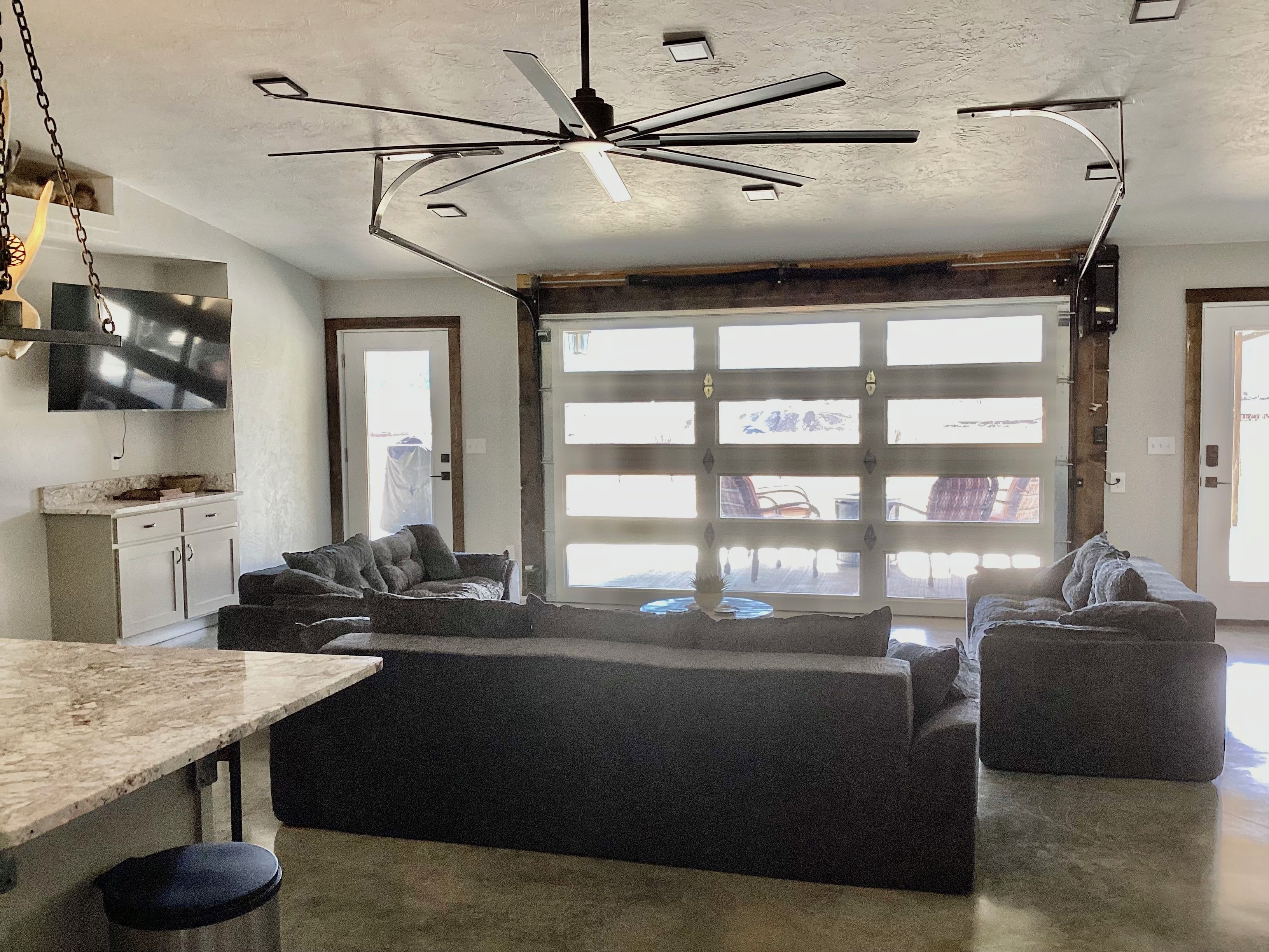 A modern kitchen with a large island, a ceiling fan, and a TV mounted on the wall.