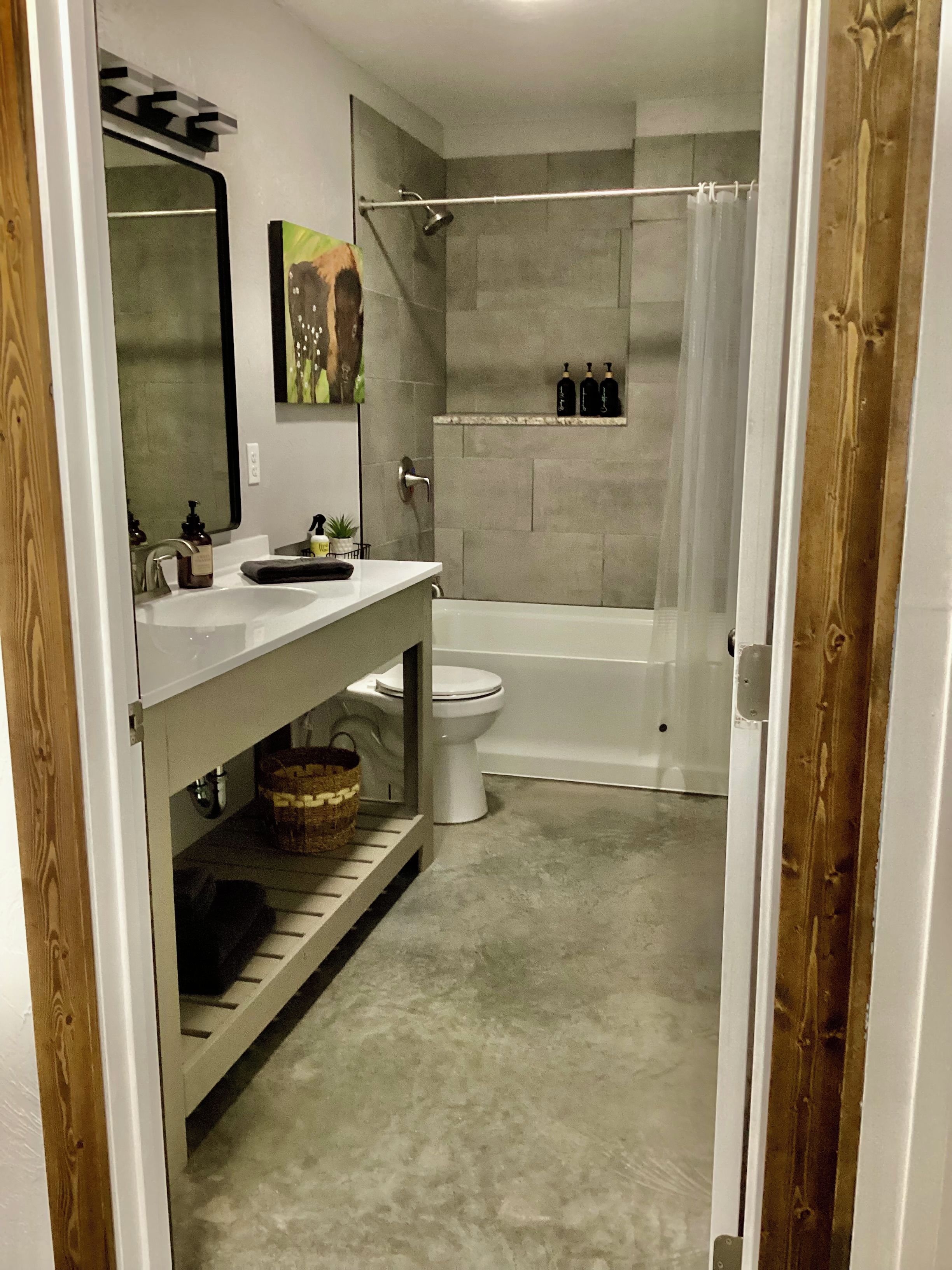 A bathroom with a white sink, toilet, and bathtub. There is a shower curtain and a shelf with bottles.