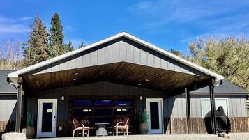 A building with a covered garage, two chairs outside, and a person in a hooded jacket.
