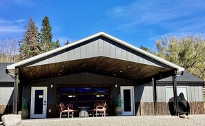 Ein Gebäude mit überdachter Garage, zwei Stühlen draußen und einer Person in einer Kapuzenjacke.