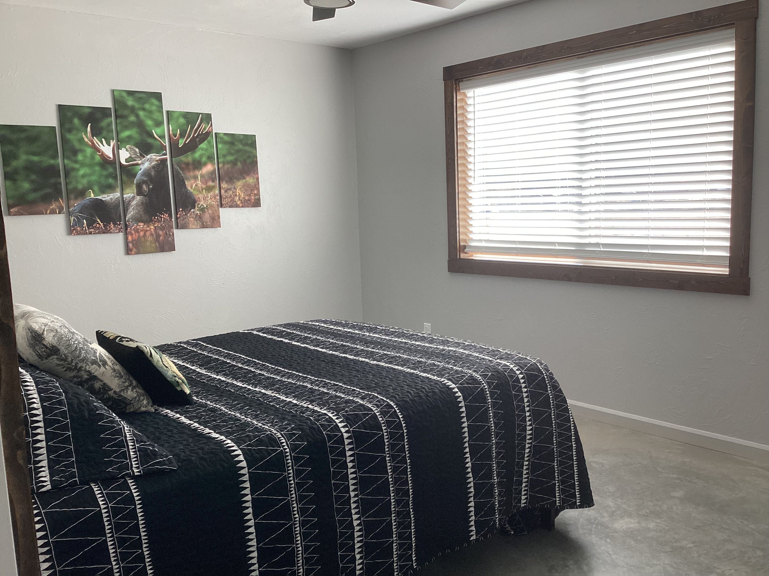 Un dormitorio con una cama, un ventanal con persianas y tres cuadros colgados en la pared.