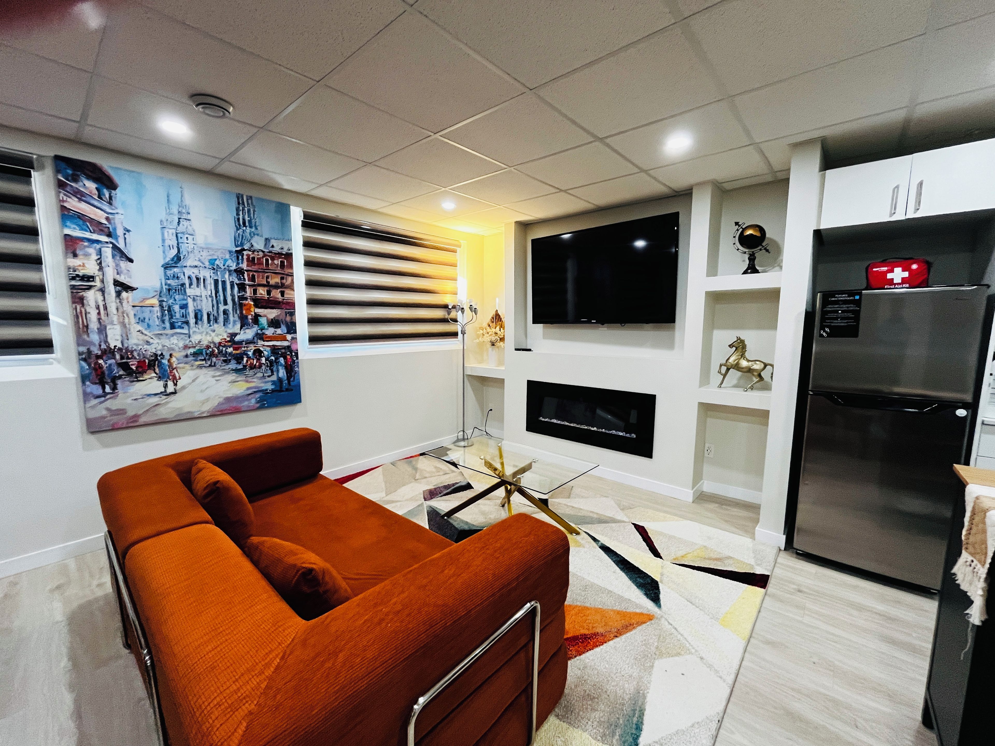 Ein modernes Wohnzimmer mit einer Couch, einem Flachbildfernseher, einem Kühlschrank und einem Bild an der Wand.